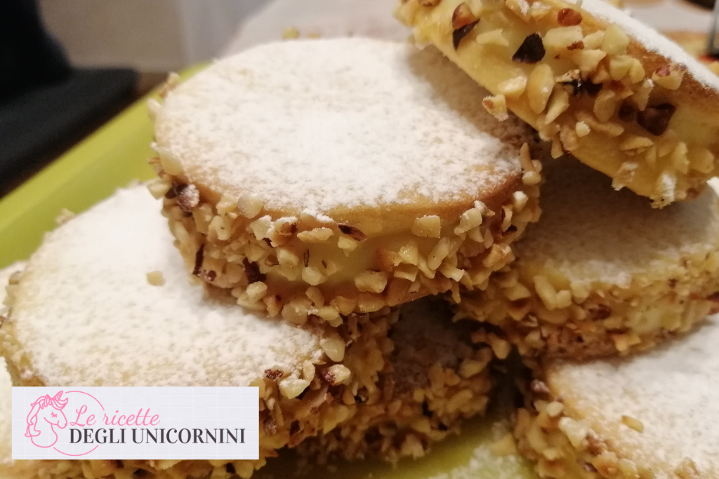 gruppo di dolcetti di pasta frolla, dalla forma a ruota. Lungo il lato della farcitura, attorno alla crema pasticcera, granella di nocciole. Sulla superficie zucchero a velo