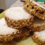 gruppo di dolcetti impilati e sovrapposti. Ogni dolcetto è un monoporzione costituito da due piccoli dischi di frolla farciti con crema. Lungo il lato della farcitura, granella di nocciole