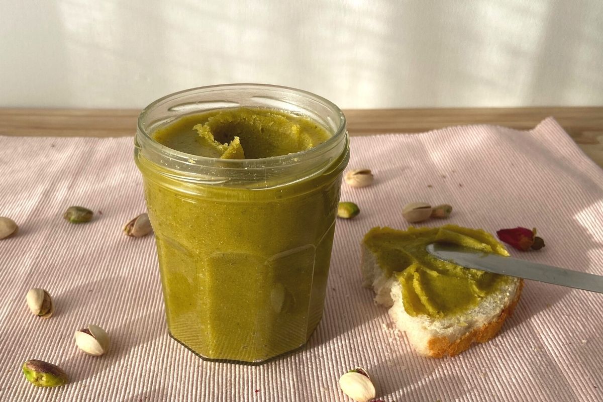 vasetto di vetro su tovaglia rosa crema verde spalmabile ai pistacchi con pane